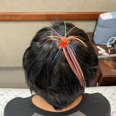 The back of Irene’s head with brightly colored EEG electrode wires gathered in her hair.