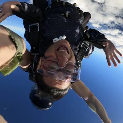 Irene upside down in freefall during a skydive, arms spread against a blue sky.
