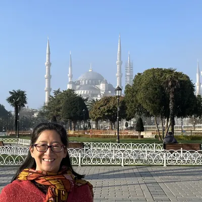 Irene in a red scarf in front of a domed mosque with tall minarets, Istanbul.
