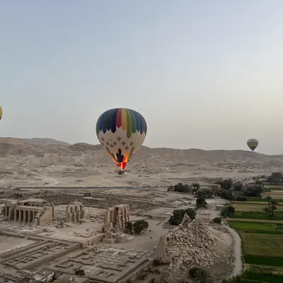 Hot-air balloons rising at dawn over ancient temple ruins and green fields, Egypt.